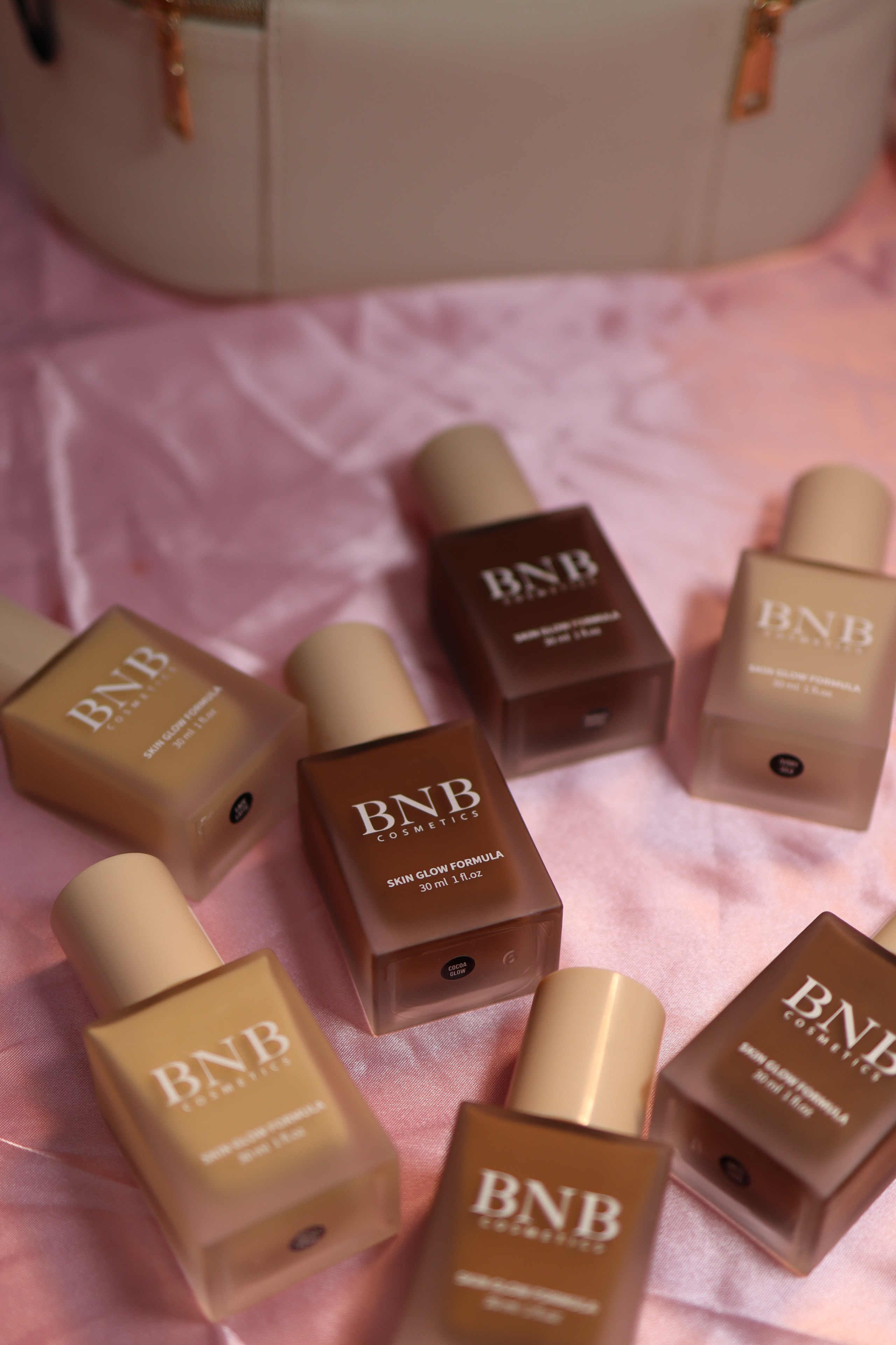 BNB Cosmetics Skin Glow Formula foundation bottles scattered on pink satin