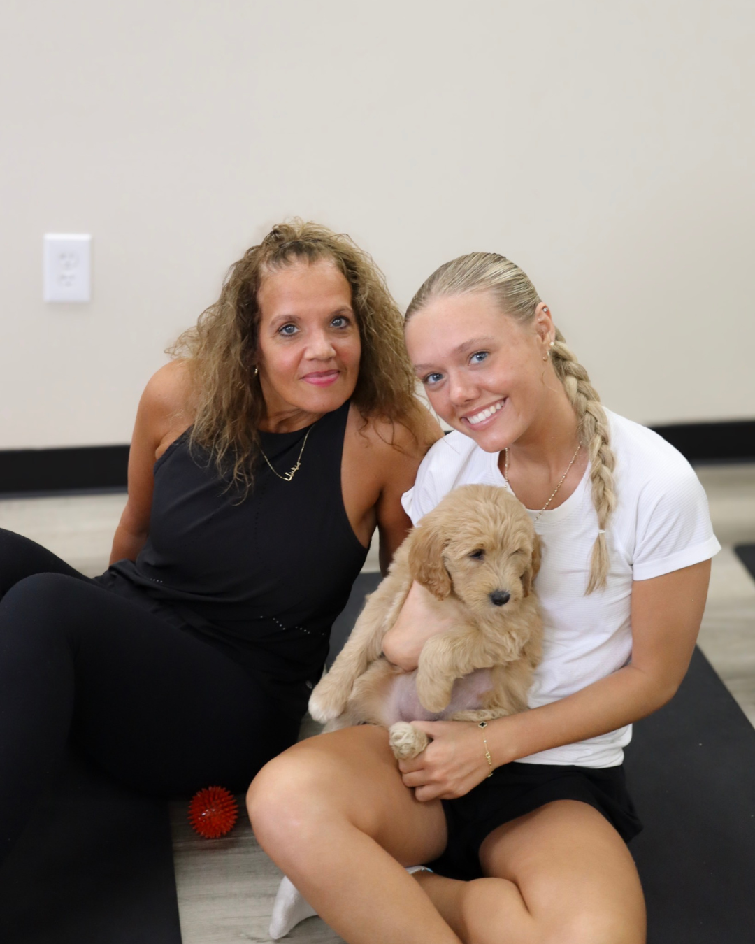 Two people posing with a golden puppy after class
