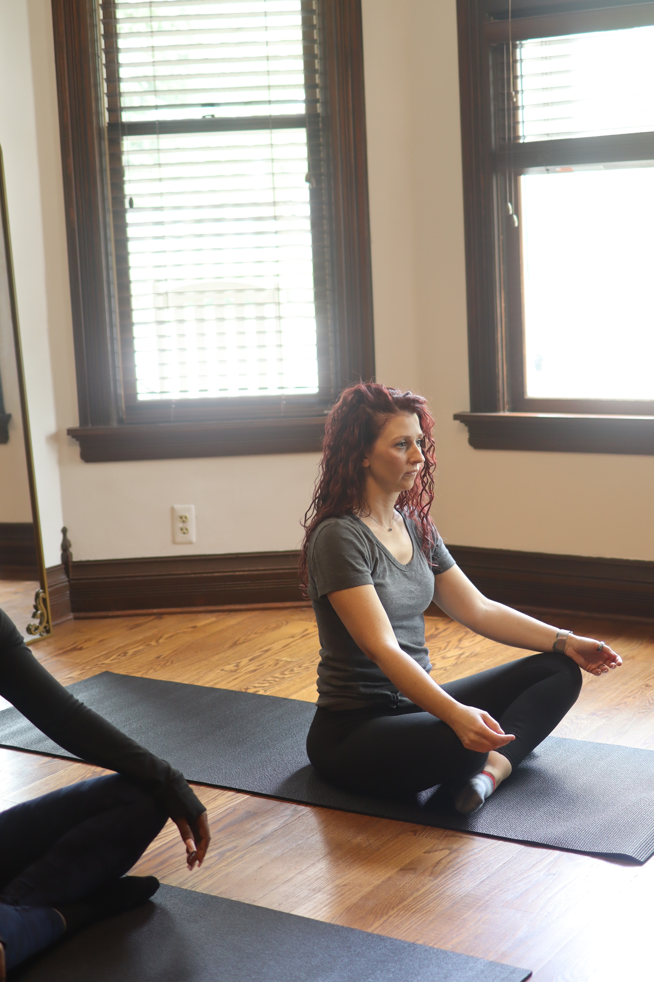 Woman stretching on yoga mat in bright studio with dark wood trim windows