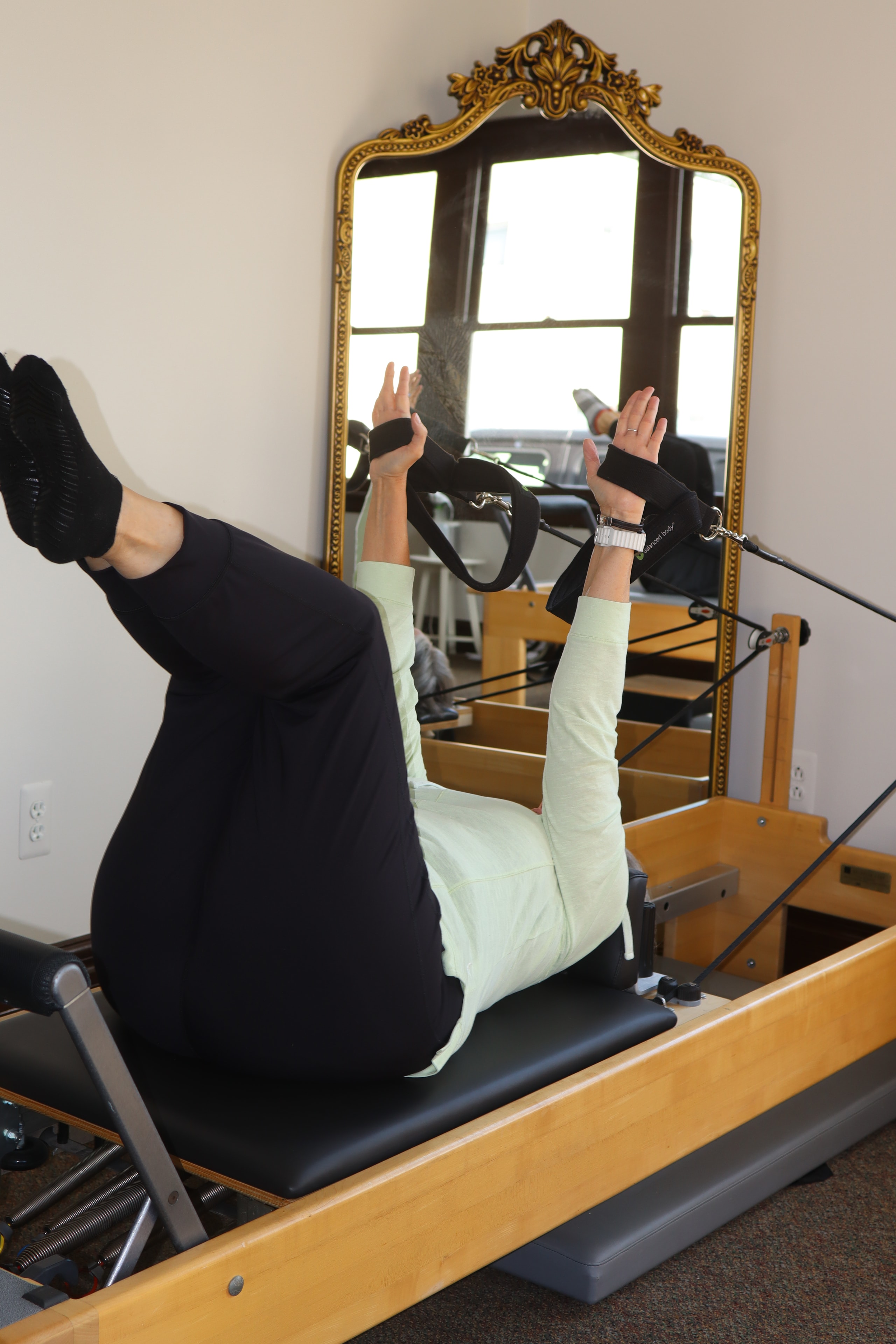 Client using Pilates reformer with instructor guidance, gold mirror in background